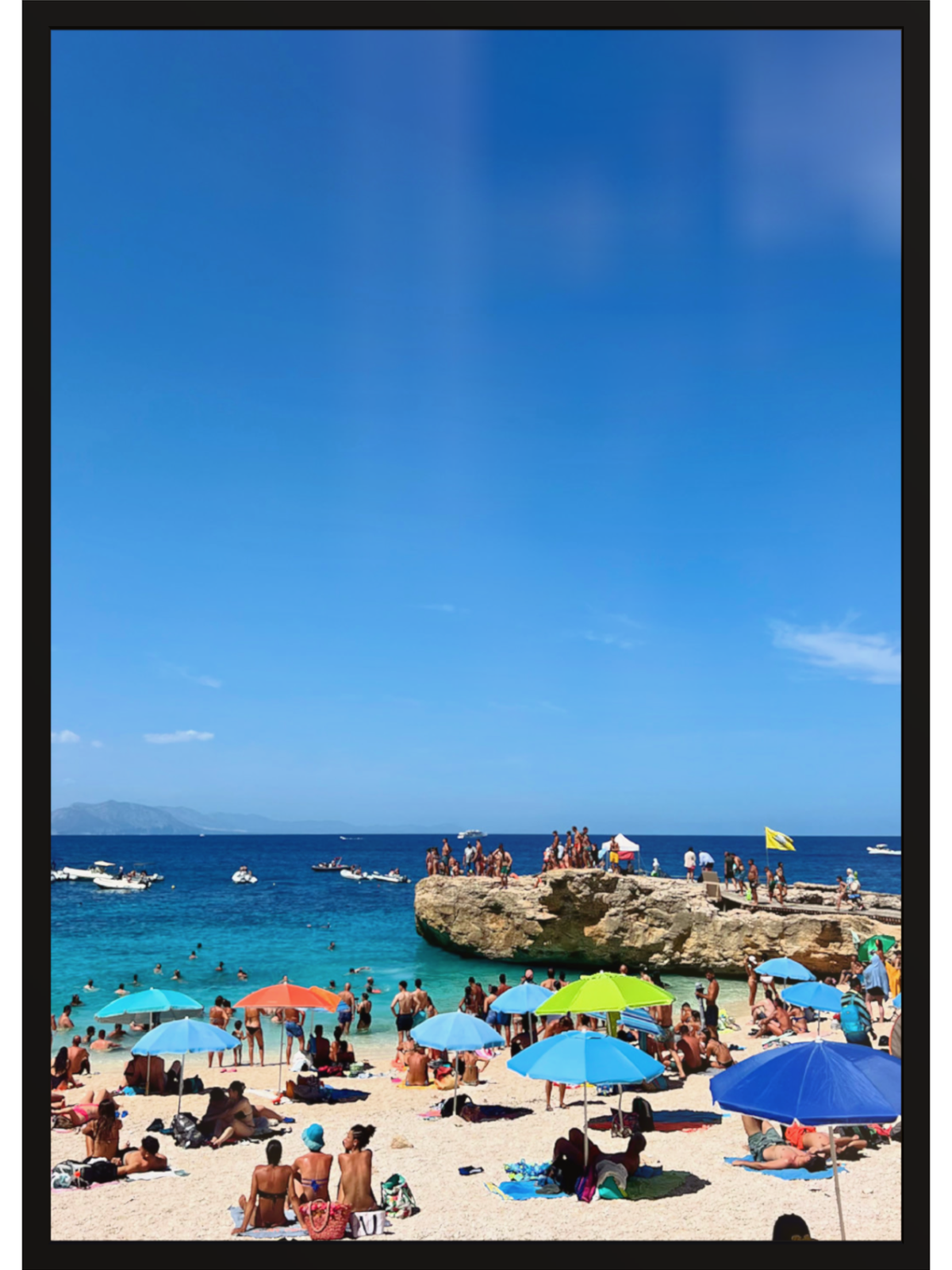 Beach scene with people under colorful umbrellas and a clear blue sky.