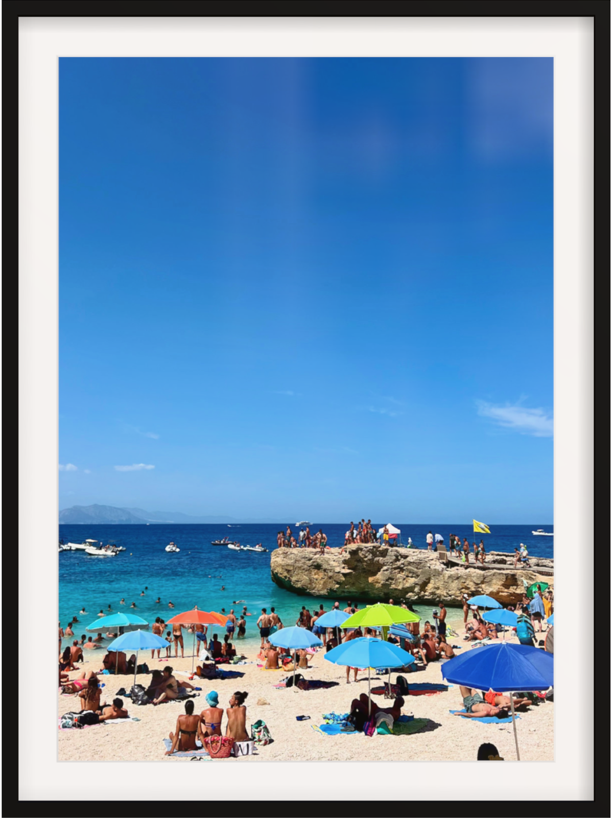 Beach scene with people under colorful umbrellas and boats in the water.