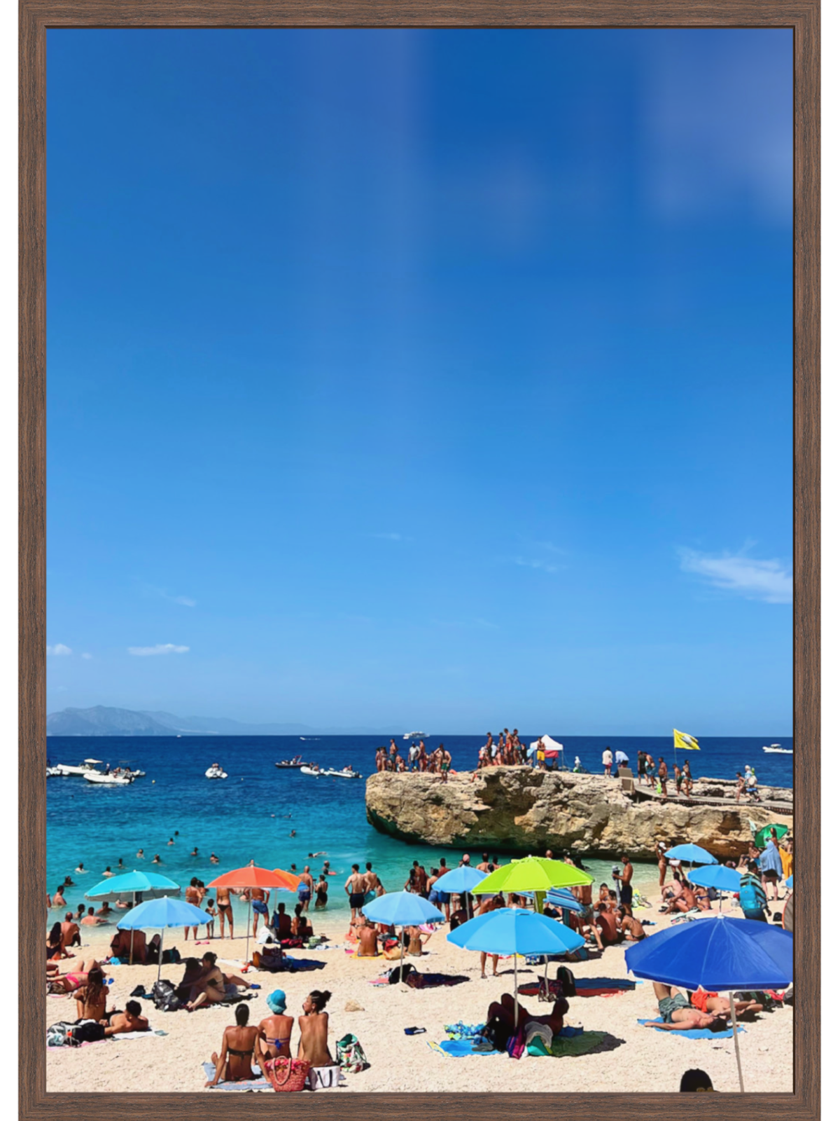 Beach scene with people, colorful umbrellas, and a clear blue sky.