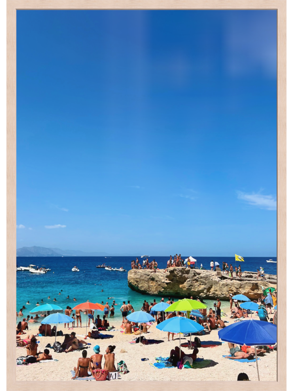 Beach scene with people, umbrellas, and boats under a clear blue sky.