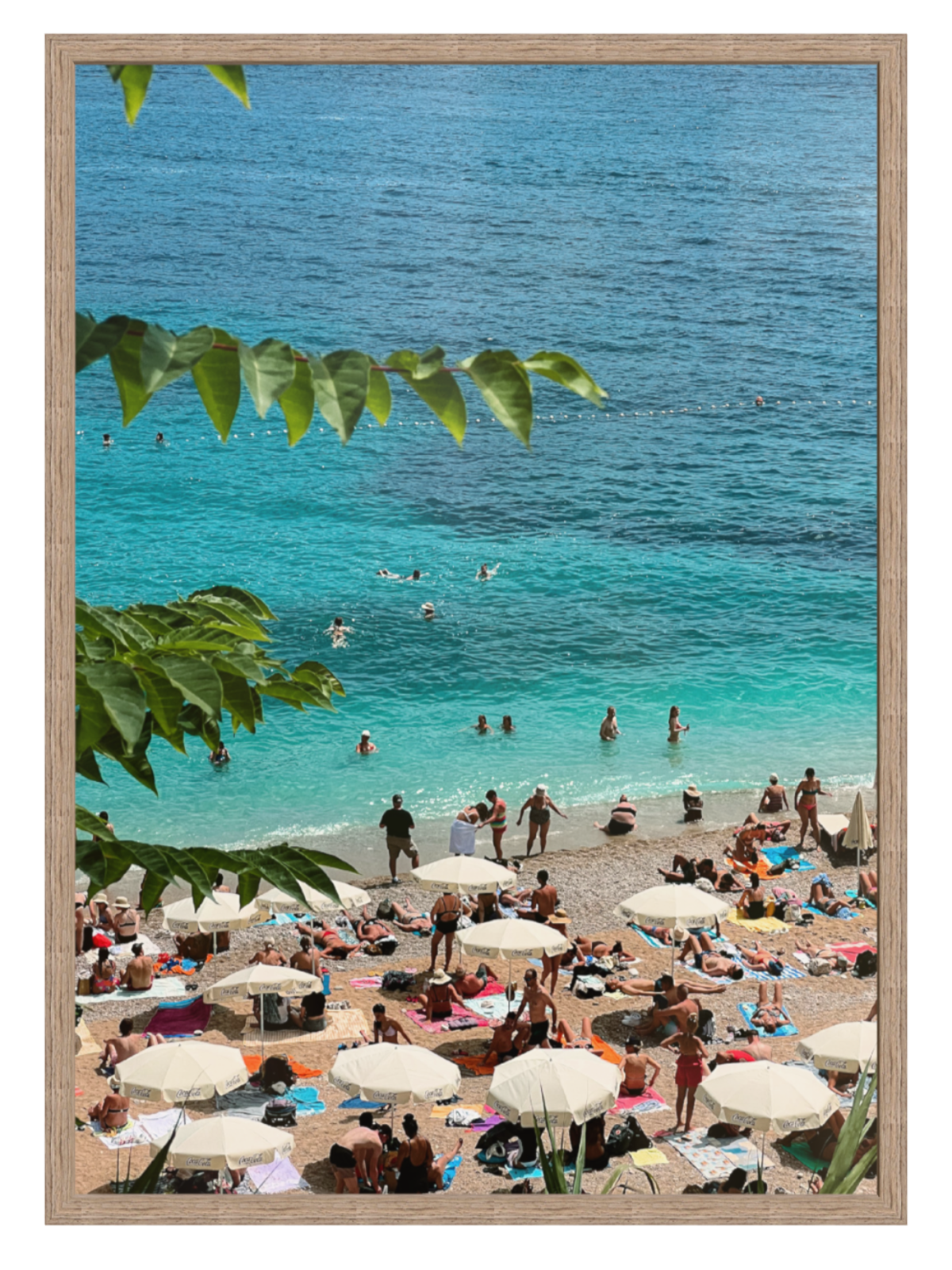 Beach scene with people, umbrellas, and turquoise water framed by green leaves. Banje Beach leaf hazel frame