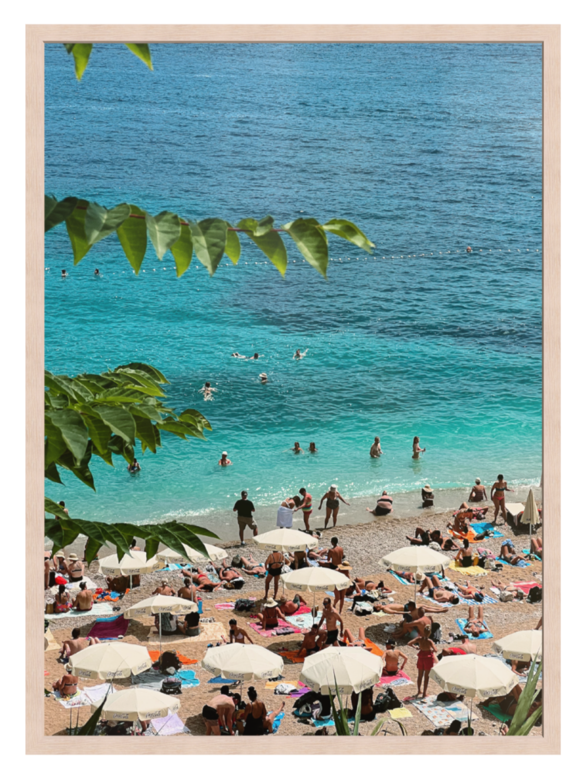 Beach scene with people, umbrellas, and clear blue water framed by green leaves. Banje Beach leaf light oak frame