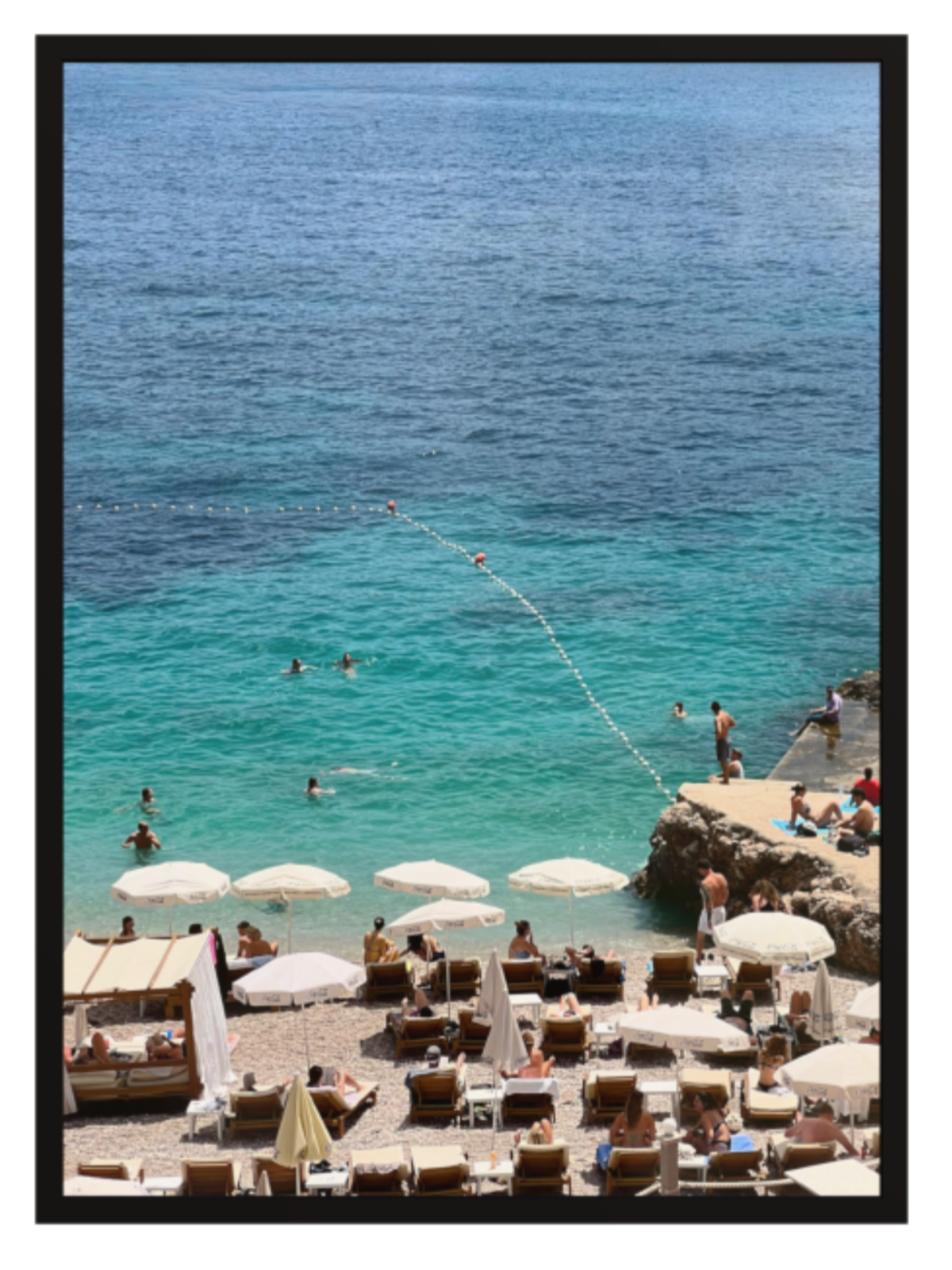 Beach scene with people, umbrellas, and clear blue water. black frame