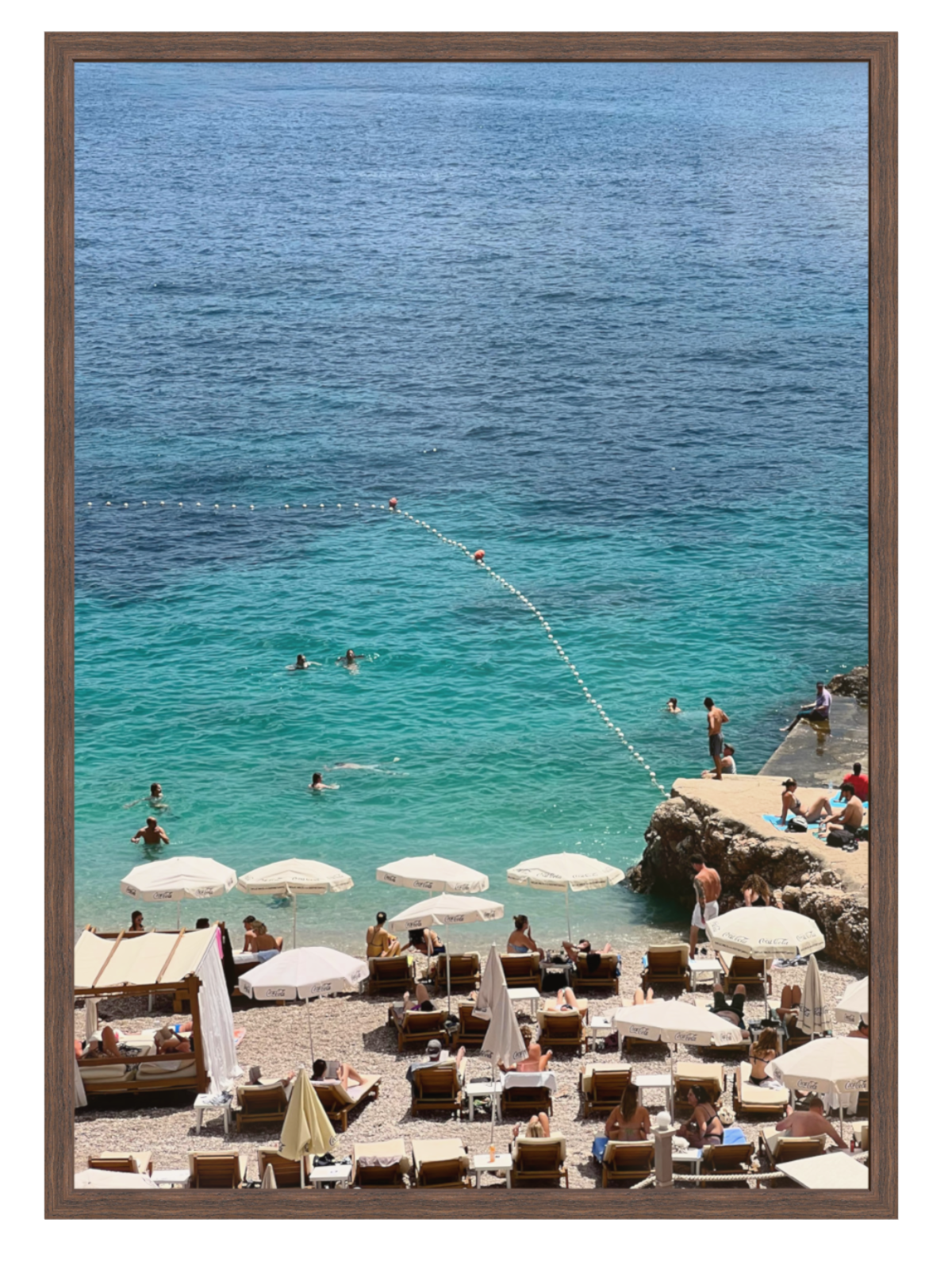 Beach scene with people, umbrellas, and lounge chairs near a body of water. chcocolate frame