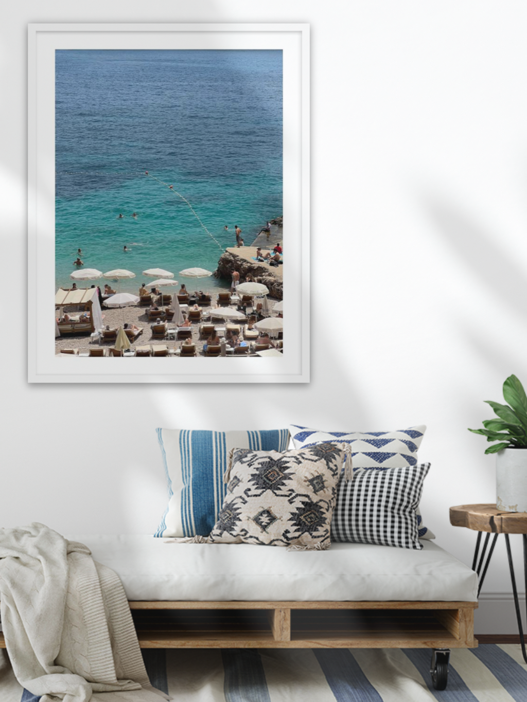 Framed beach scene print above a wooden bench with decorative pillows in a living room.