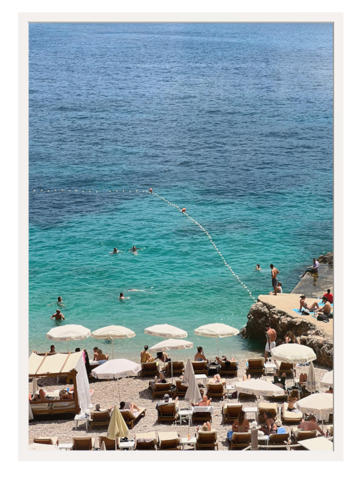 Beach scene with people, umbrellas, and chairs near a body of water. white frame