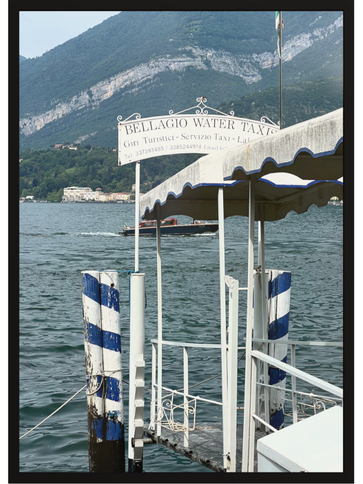 Black framed Bellagio Water Taxi art print emphasizing rocky mountains and calm lake waters