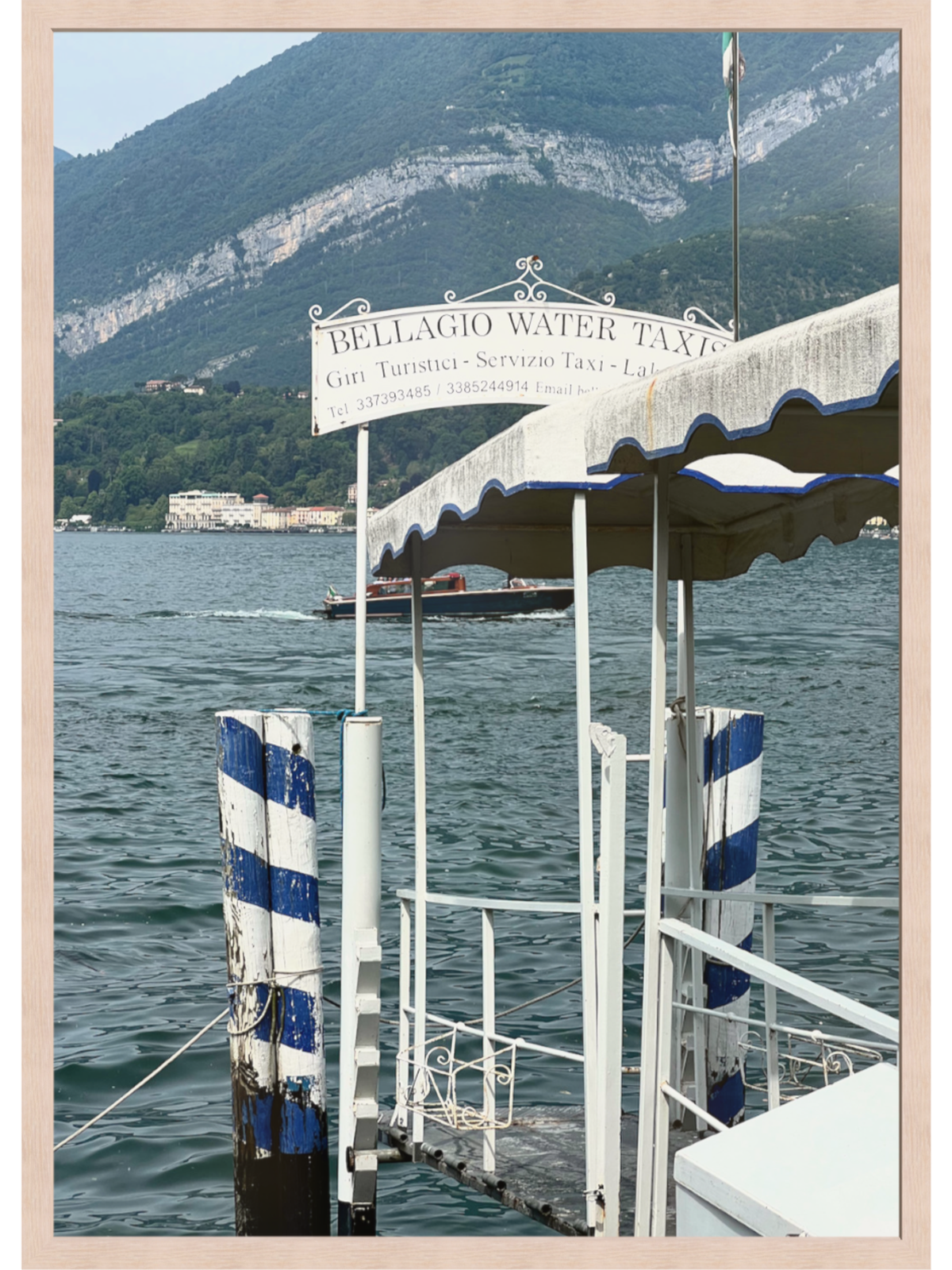 Bellagio Italy lakeside jetty art print with blue striped pilings and water taxi sign in light wood frame