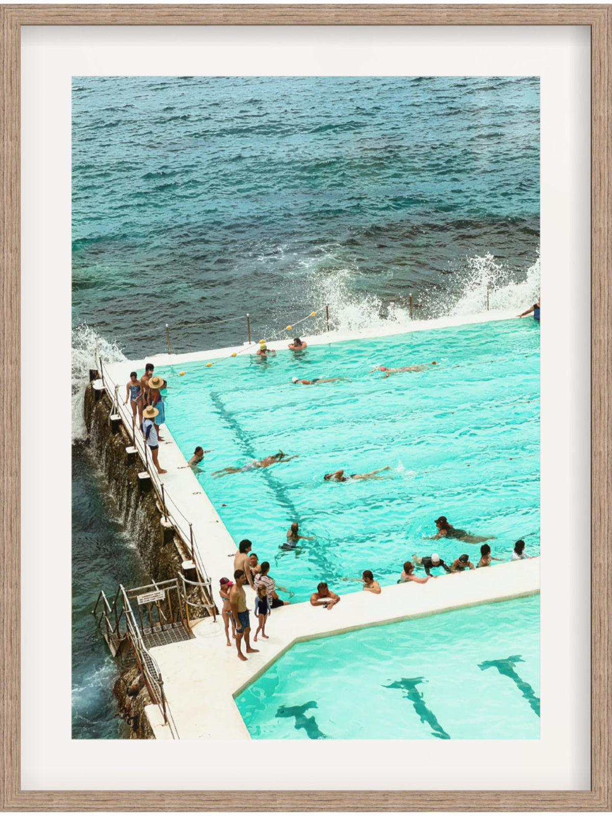 People enjoying a pool by the ocean with a wooden frame.