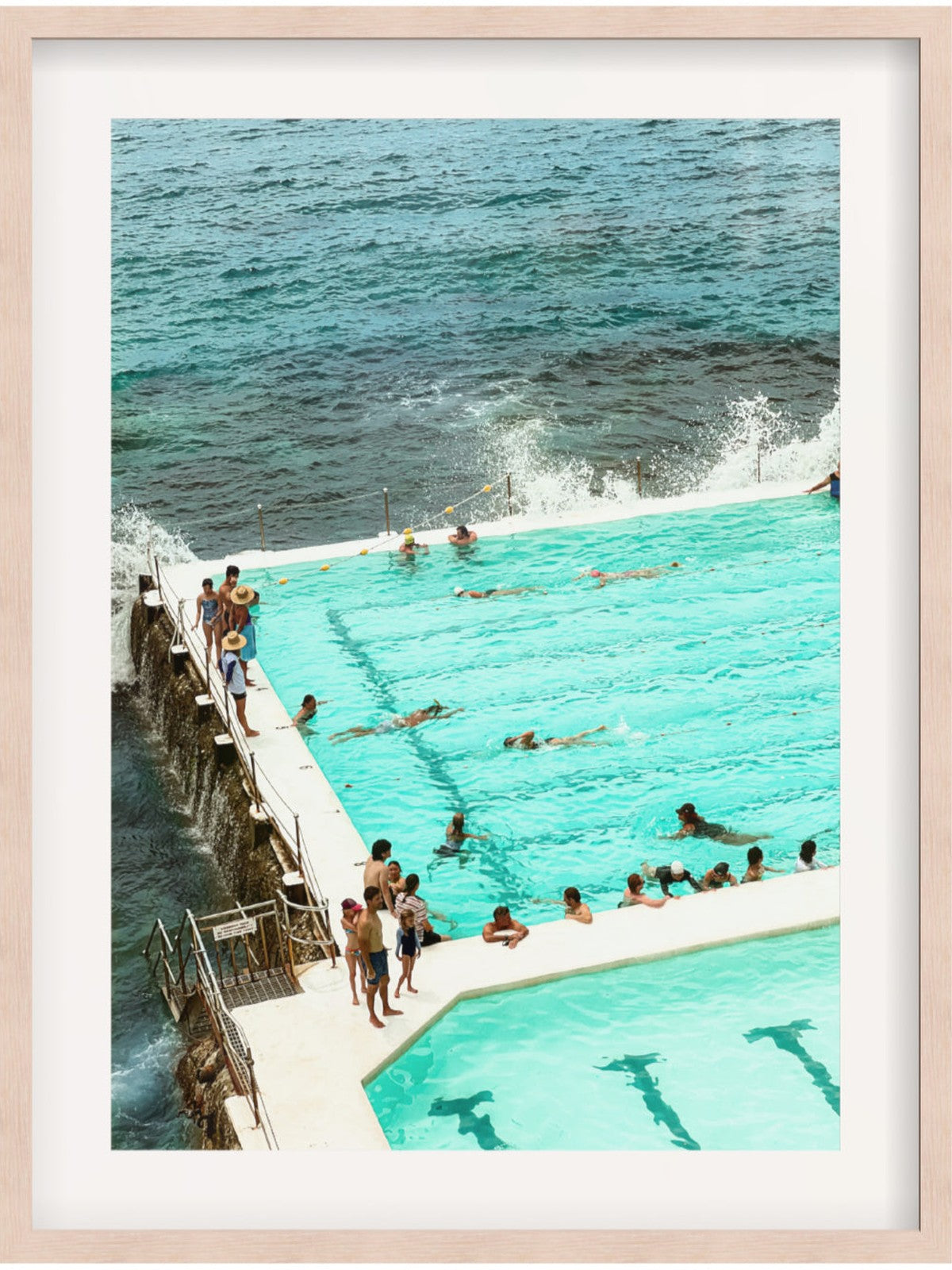 People enjoying a pool by the ocean with a wooden platform.