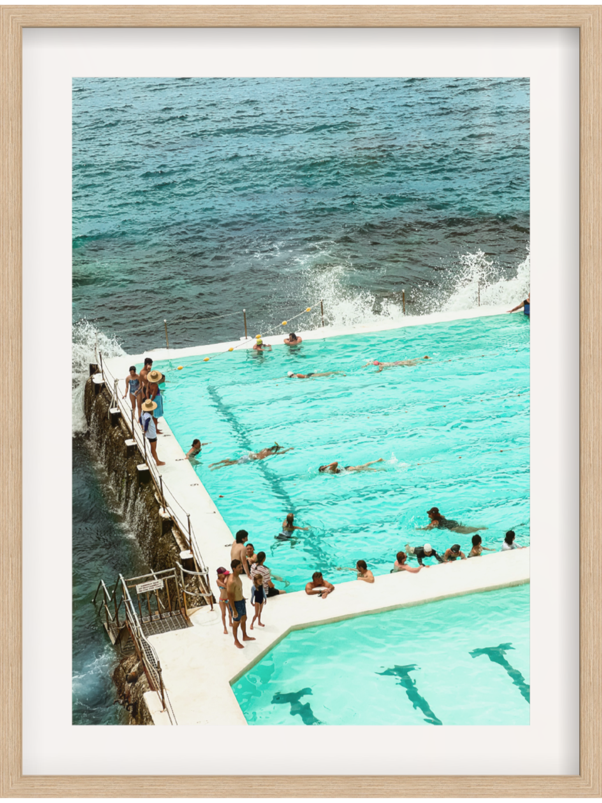 People enjoying a pool by the ocean with a wooden platform.