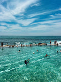 People swimming in a pool with ocean view under a blue sky.
