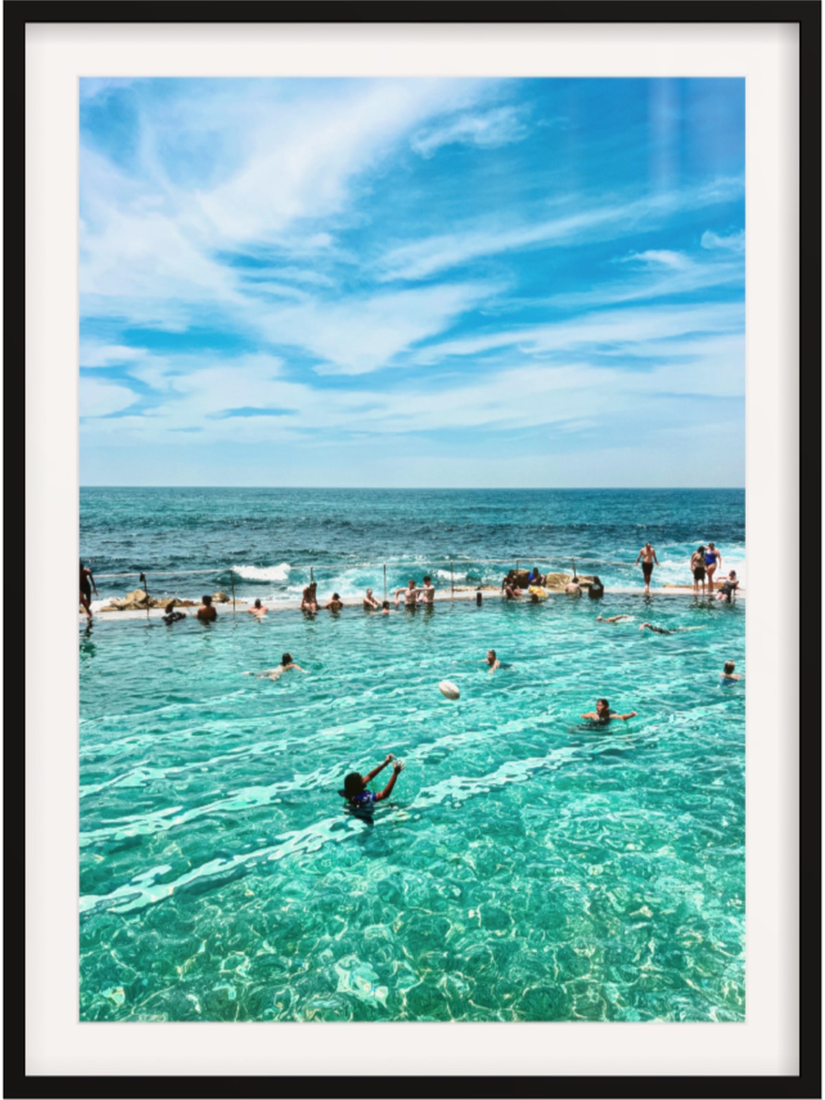 People swimming in a pool with ocean view under a blue sky.