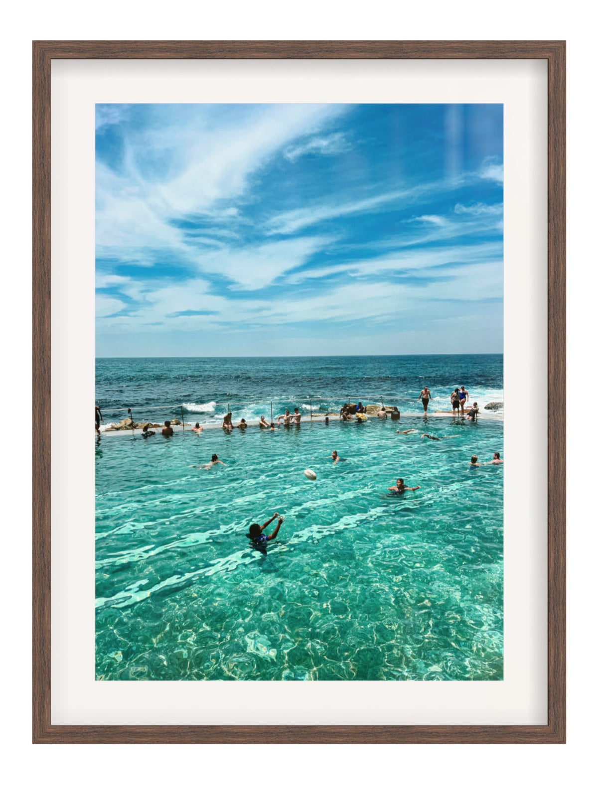 People swimming in a pool with ocean view under a blue sky.