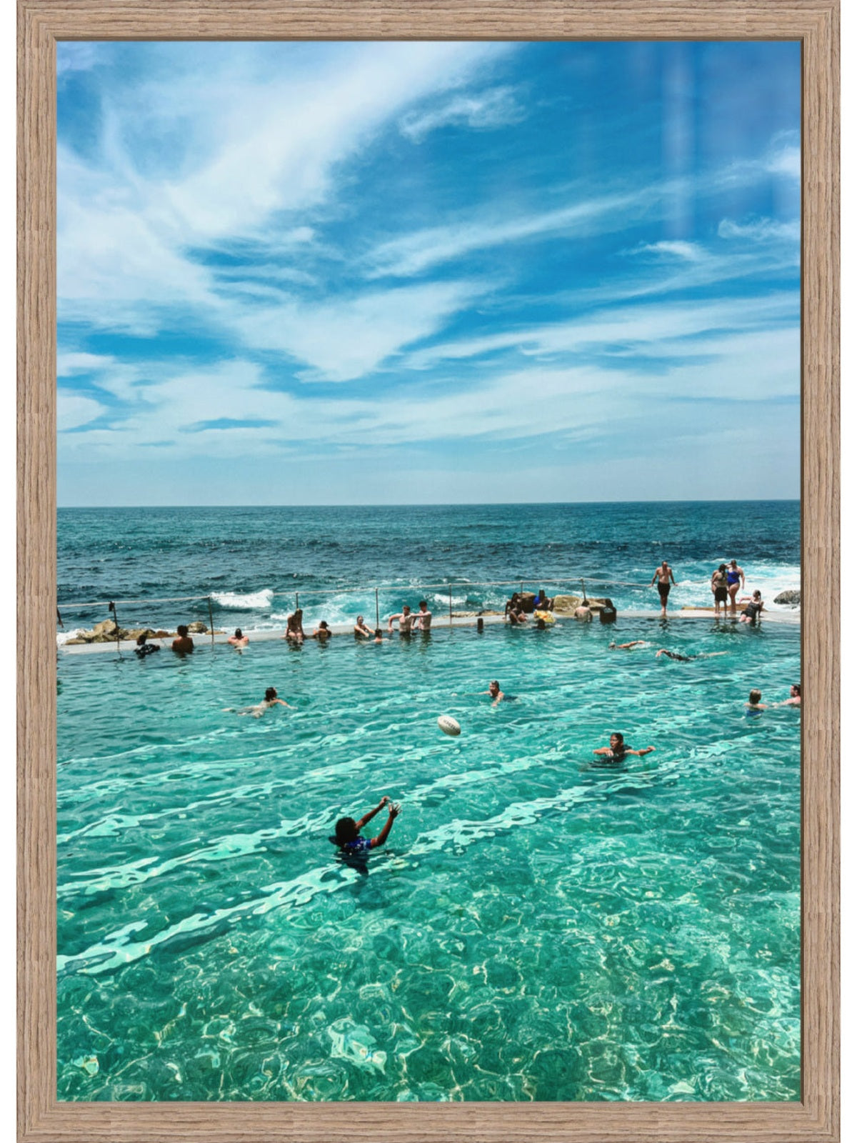 People swimming in a pool with ocean view under a blue sky.
