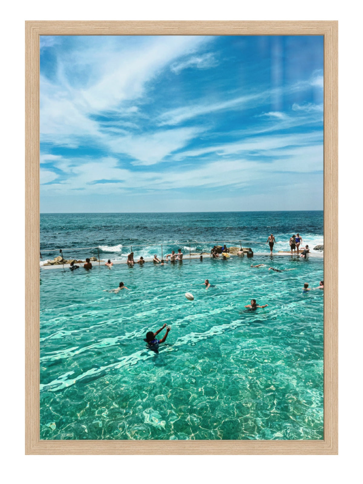 People swimming in a pool with ocean view under a blue sky.