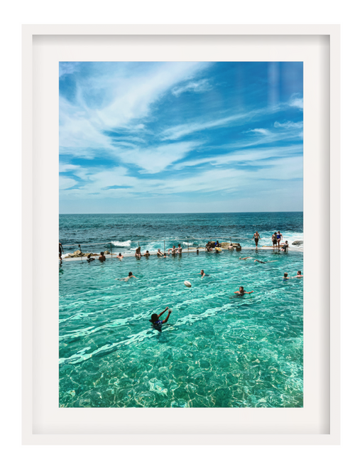 People swimming in a pool with ocean view under a blue sky.