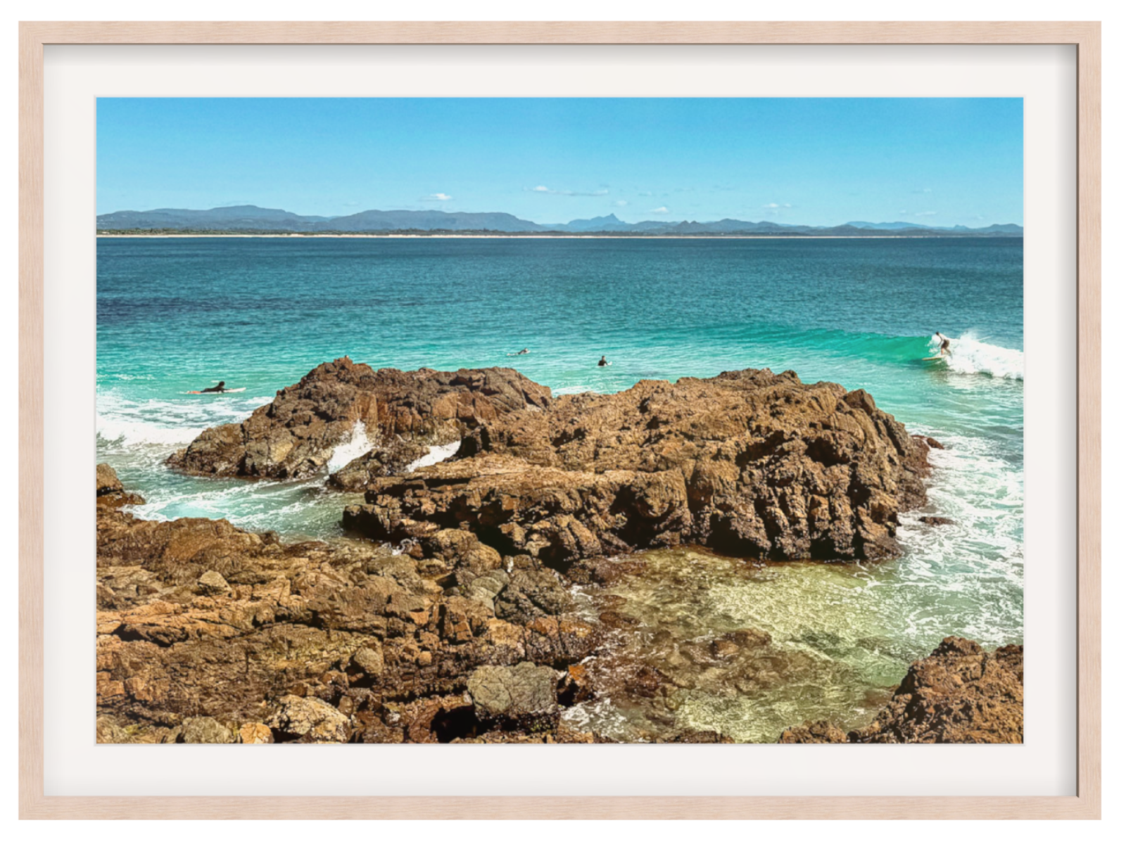 Framed photograph of a rocky coastline with clear blue water and distant mountains.