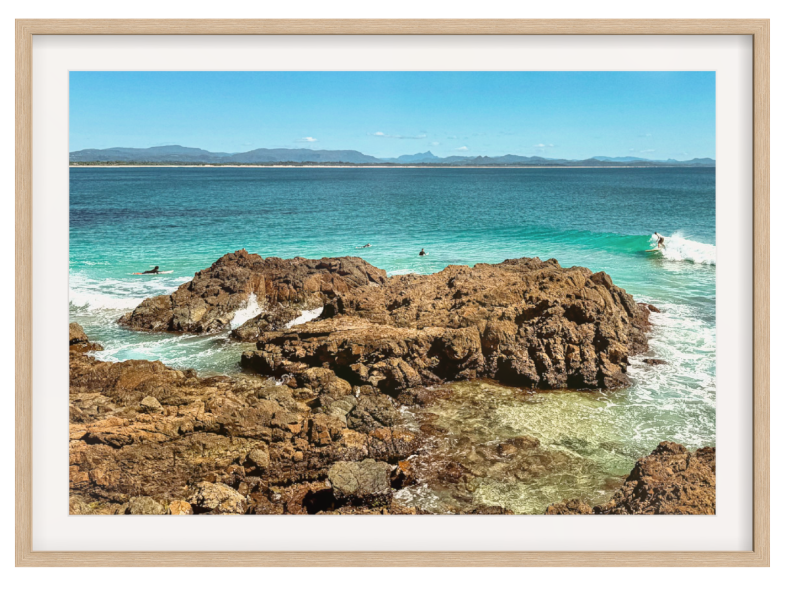 Framed photograph of a rocky coastline with clear blue water and distant mountains.