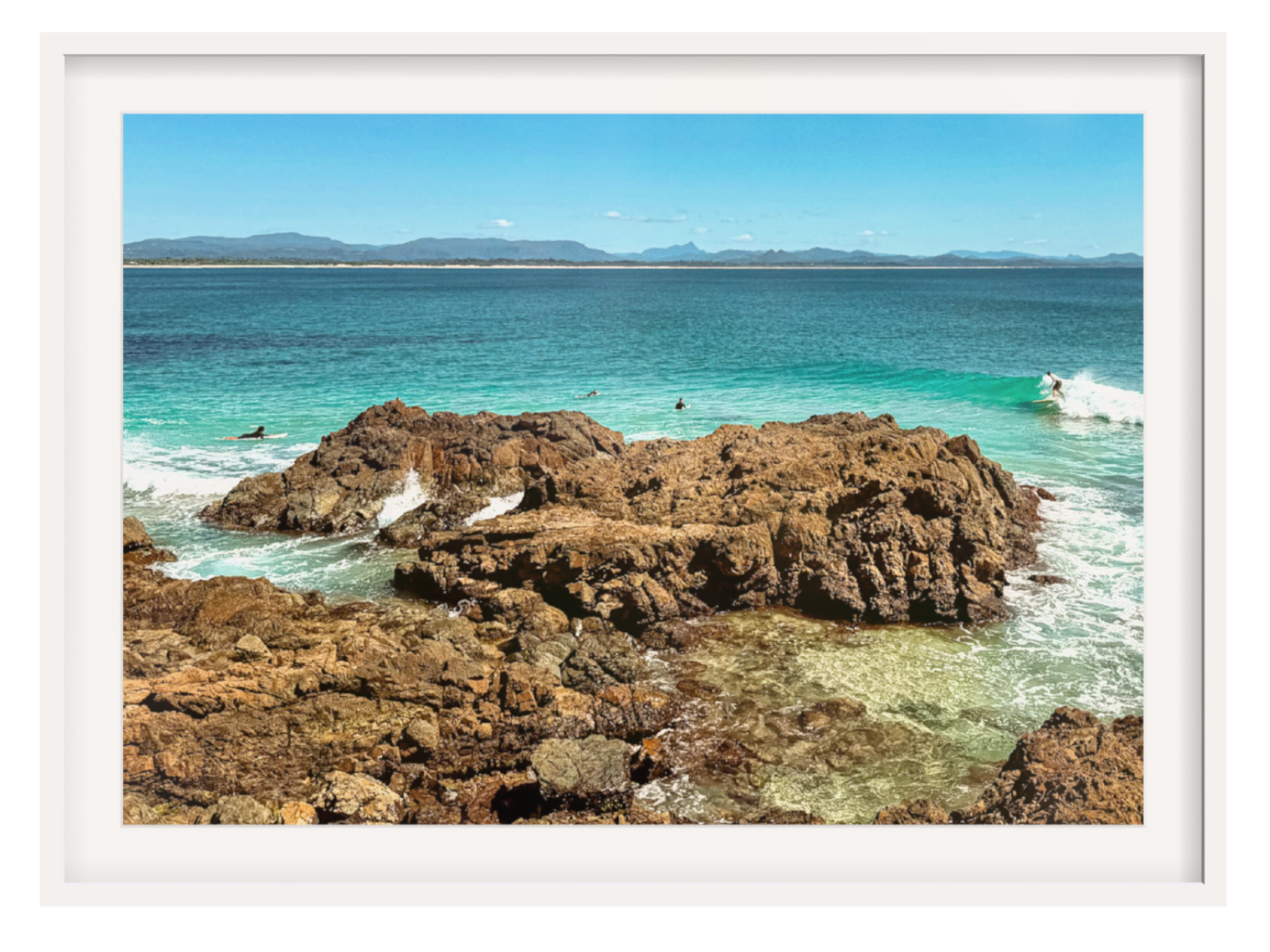 Framed photograph of a rocky coastline with clear blue water and distant mountains.