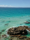 Clear blue ocean with people swimming and rocks in the foreground