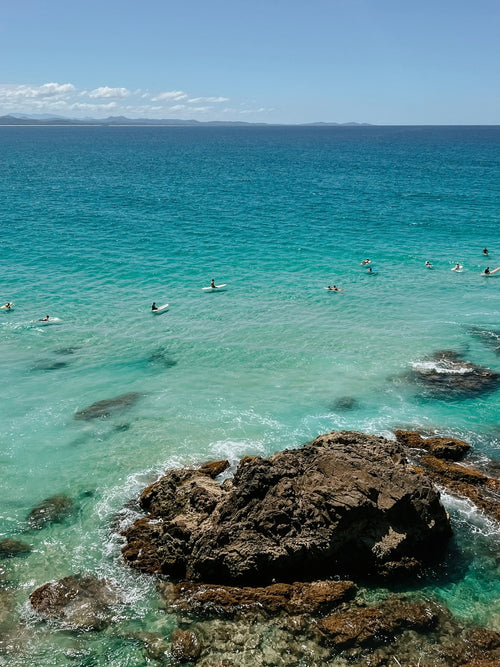 Clear blue ocean with people swimming and rocks in the foreground