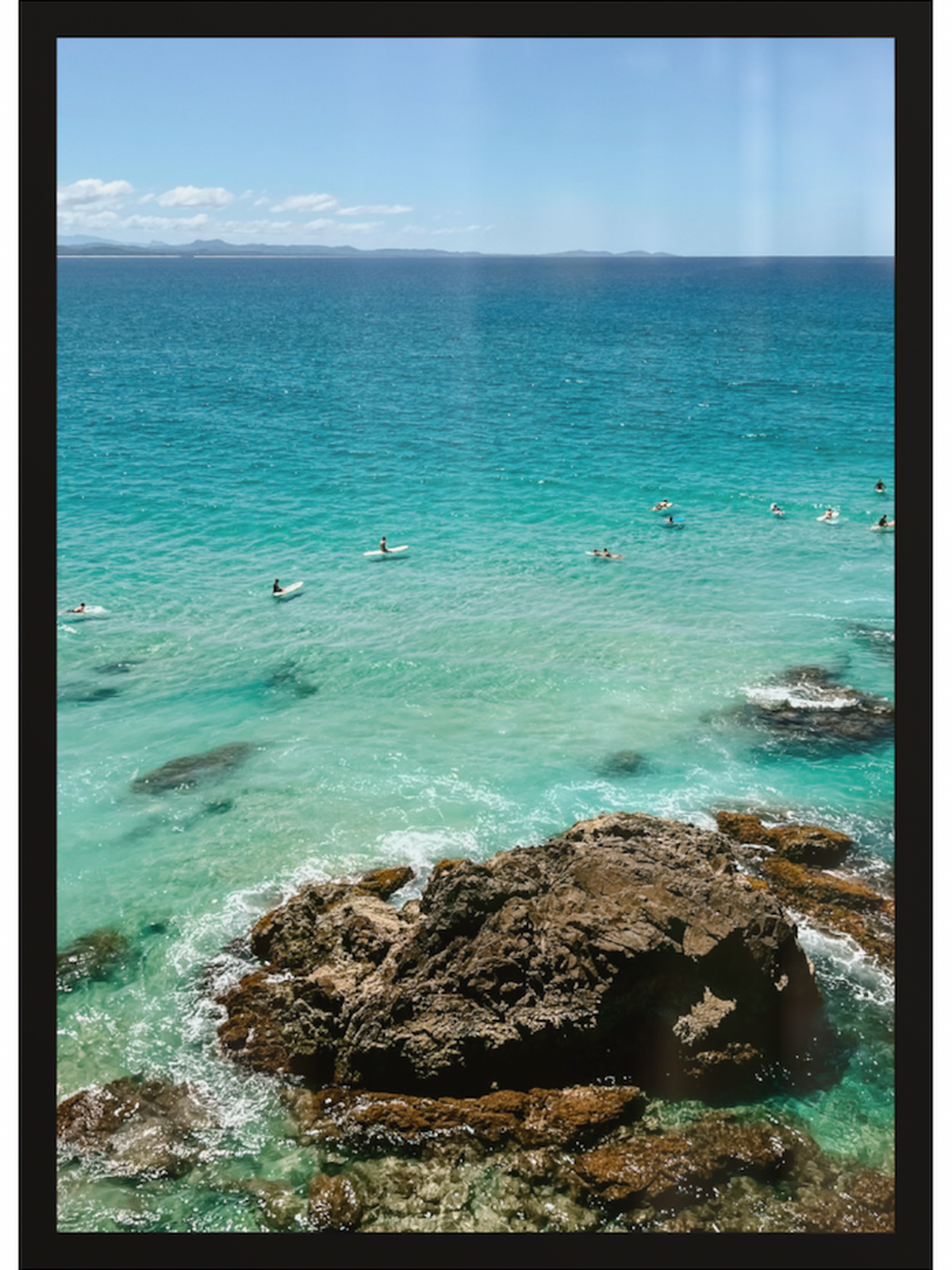 Clear blue ocean with people swimming and rocks in the foreground