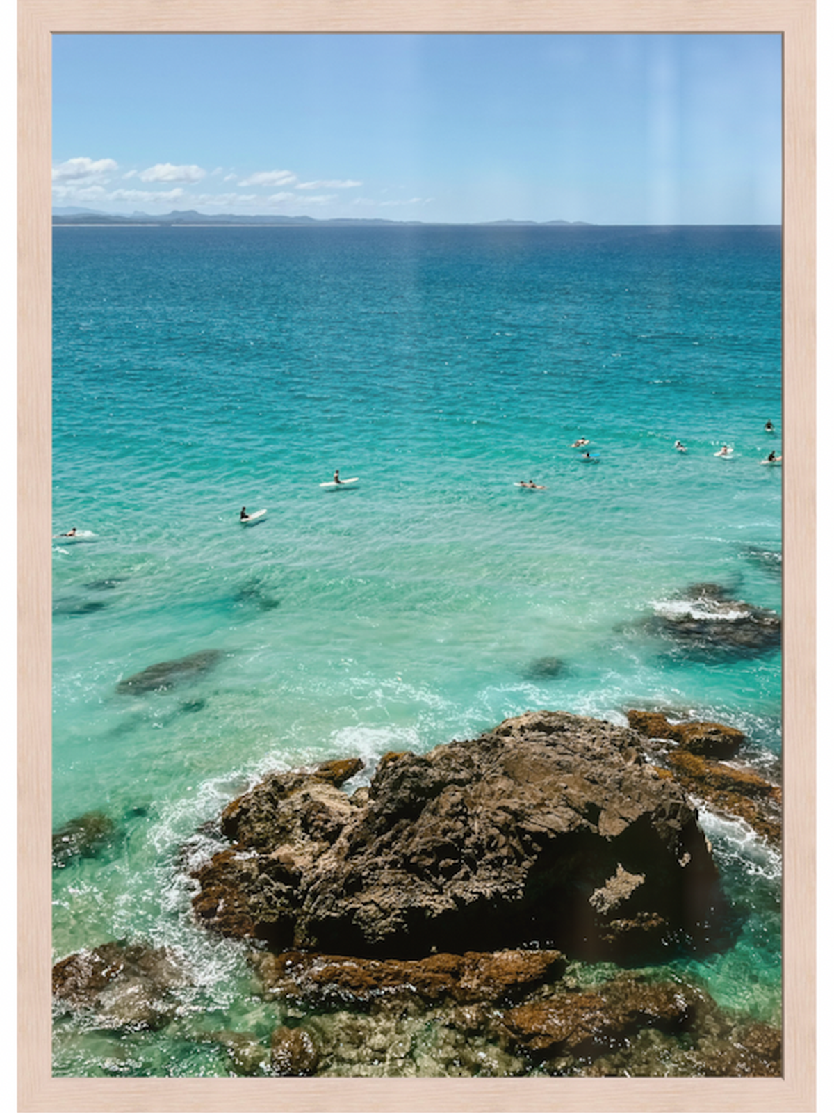 Clear blue ocean with people swimming and rocks in the foreground, framed in beige.