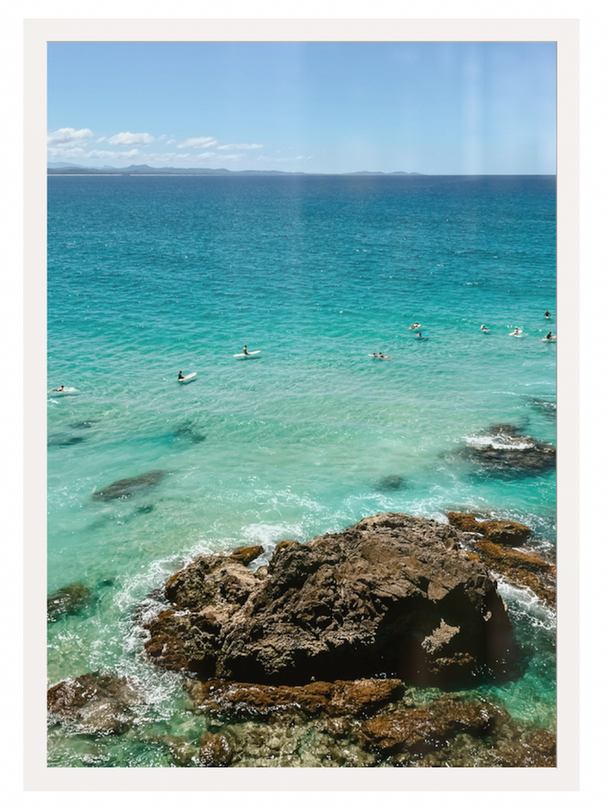 Clear blue ocean with rocky outcrops and people swimming in the distance.