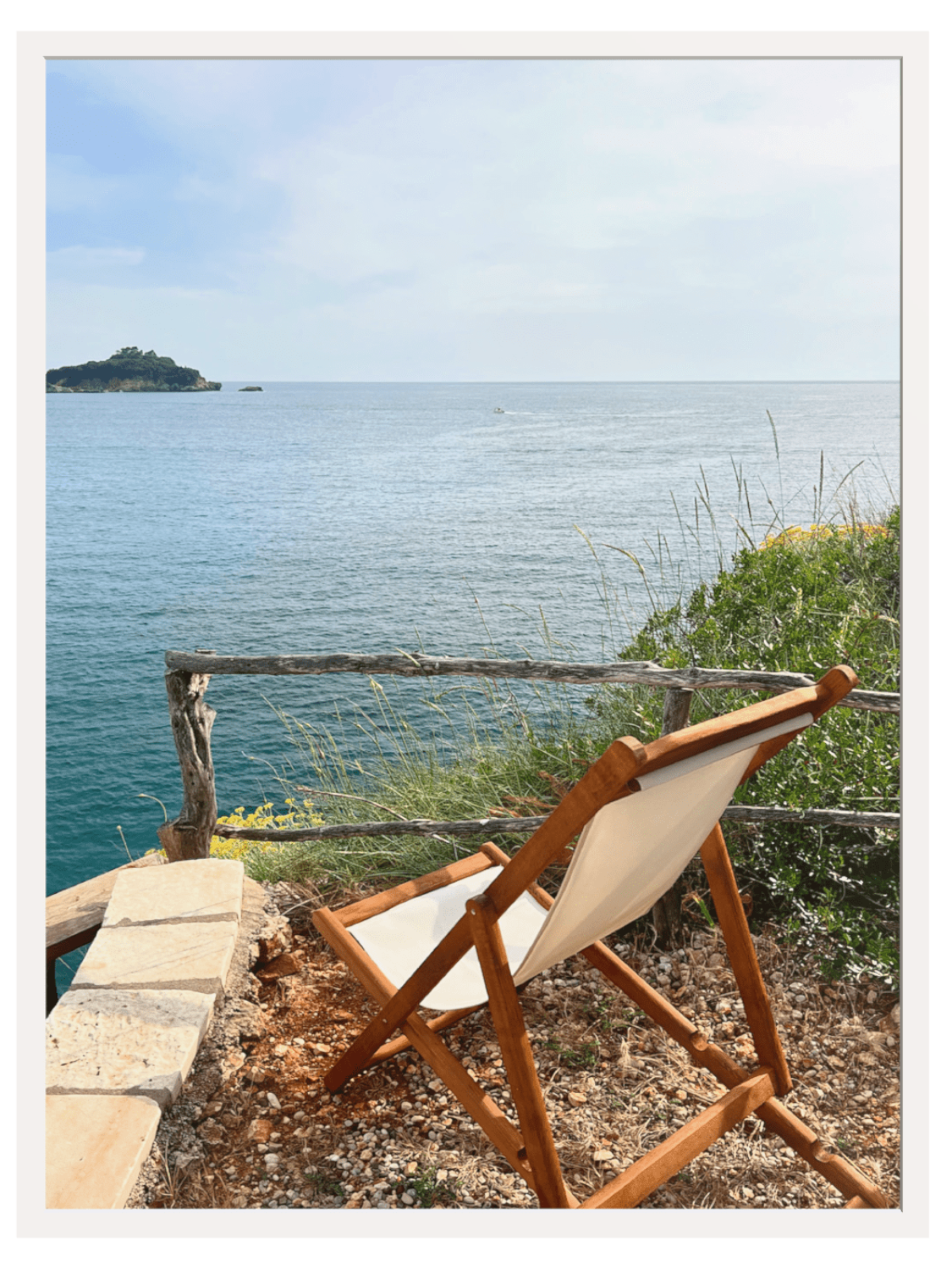 Wooden chair with white cushion overlooking a body of water and a small island.