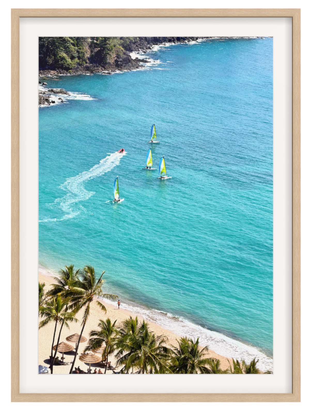 A framed photographic art print of a tropical beach scene with turquoise ocean water, three windsurfers, palm trees on the sandy shore, and a light wood frame.