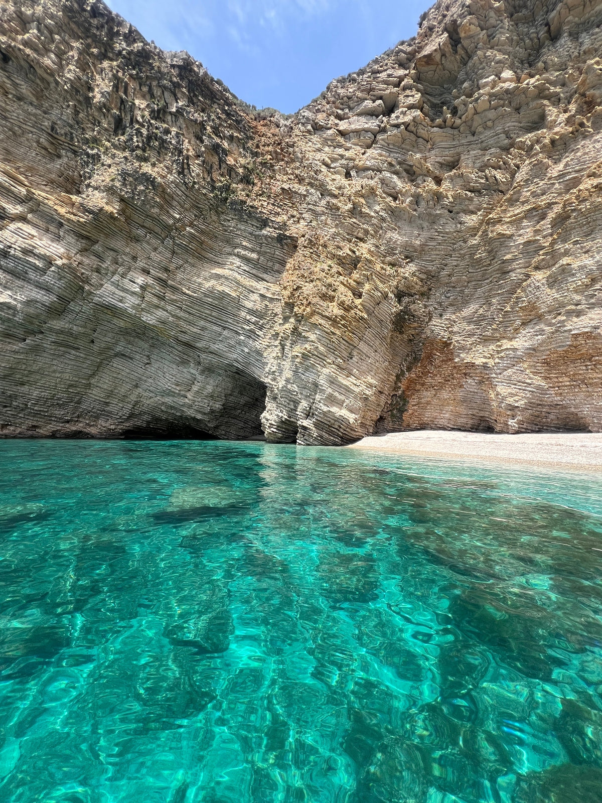 Clear turquoise water with rocky cliffs and a cave in the background