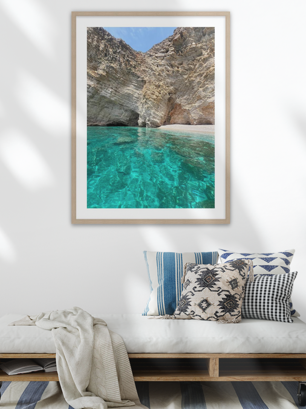 Framed artwork of a beach scene above a bench with decorative pillows.