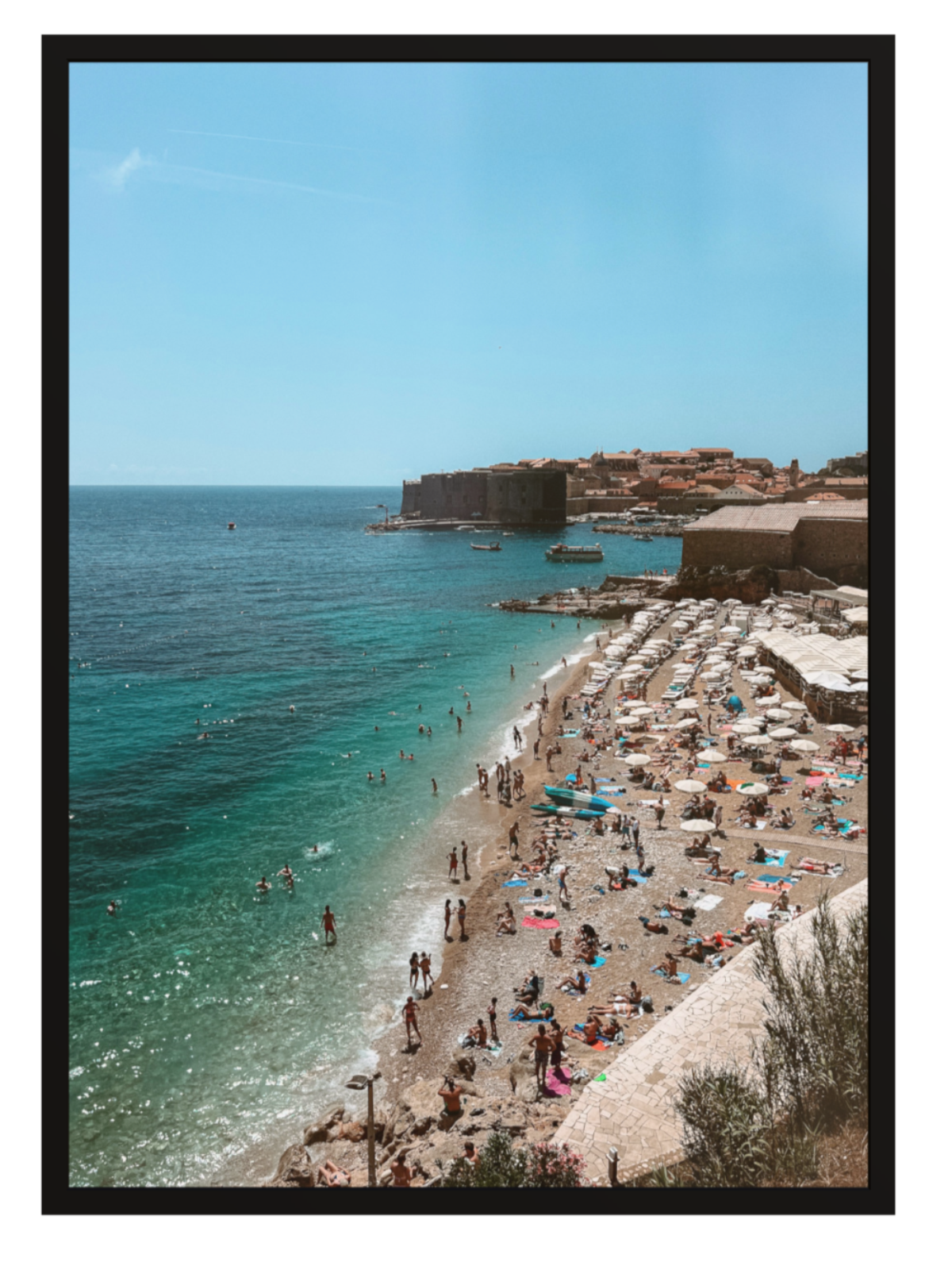 Beach scene with people and umbrellas near a castle on a hill, framed by a black border.