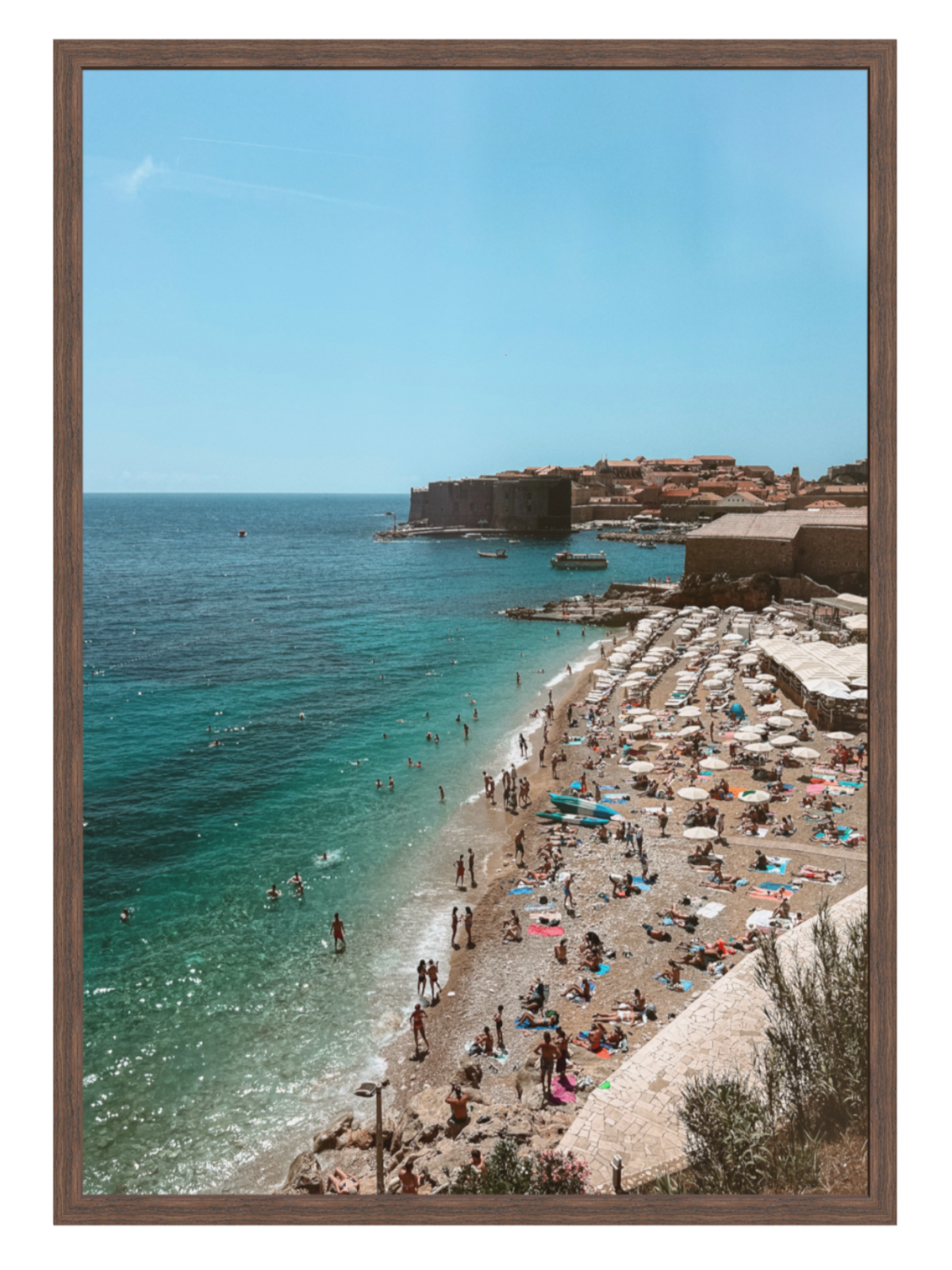 Beach scene with people and umbrellas near a castle on a hill, framed picture.