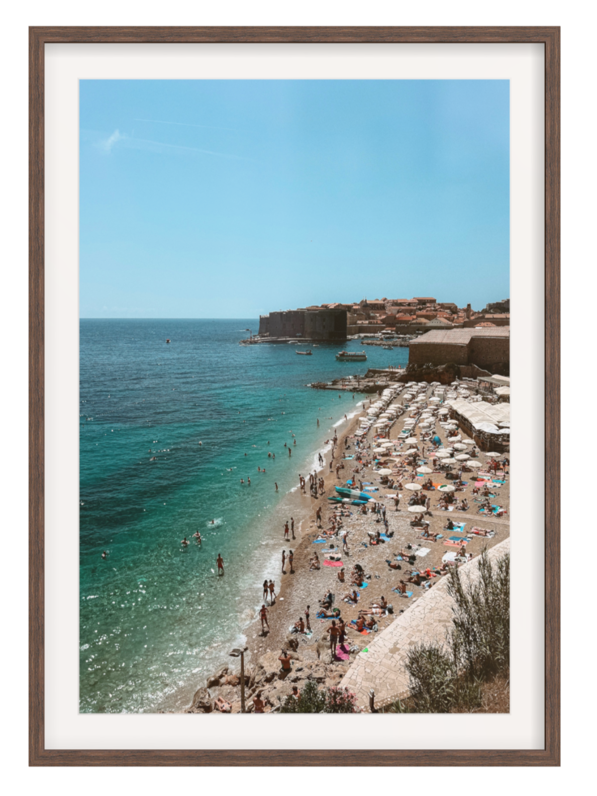 Framed photograph of a beach scene with people and umbrellas, surrounded by clear blue water and a clear sky.