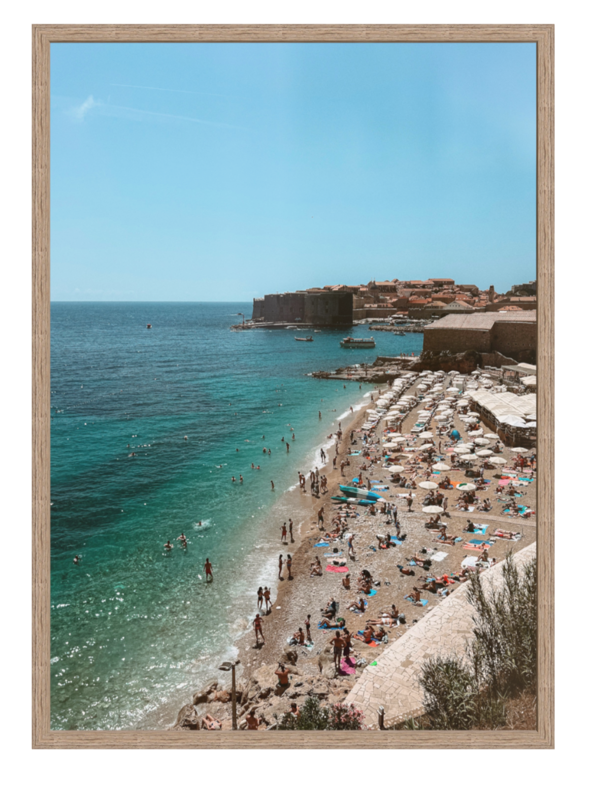 Framed photograph of a beach scene with people, umbrellas, and a clear blue sky.