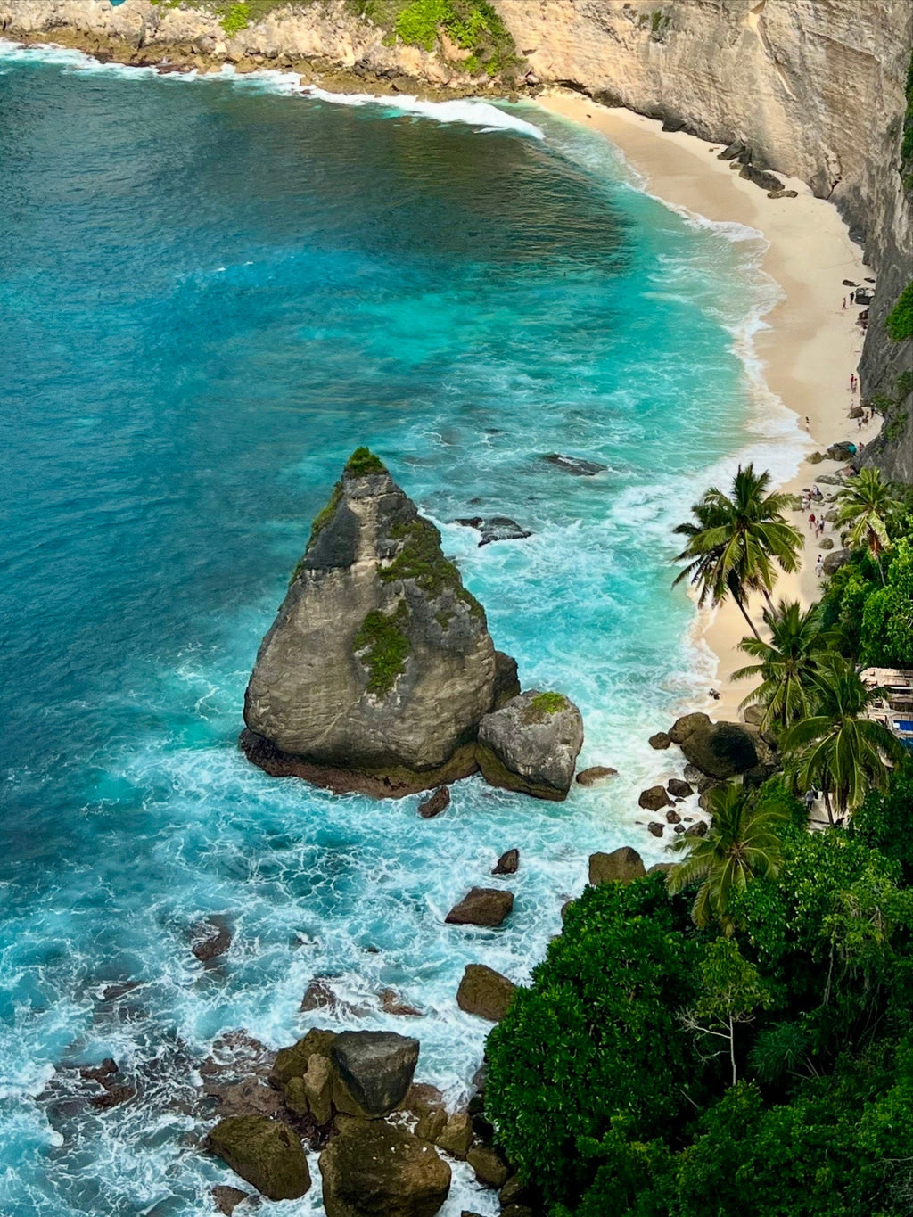 Aerial view of a rocky coastline with turquoise water and a sandy beach.