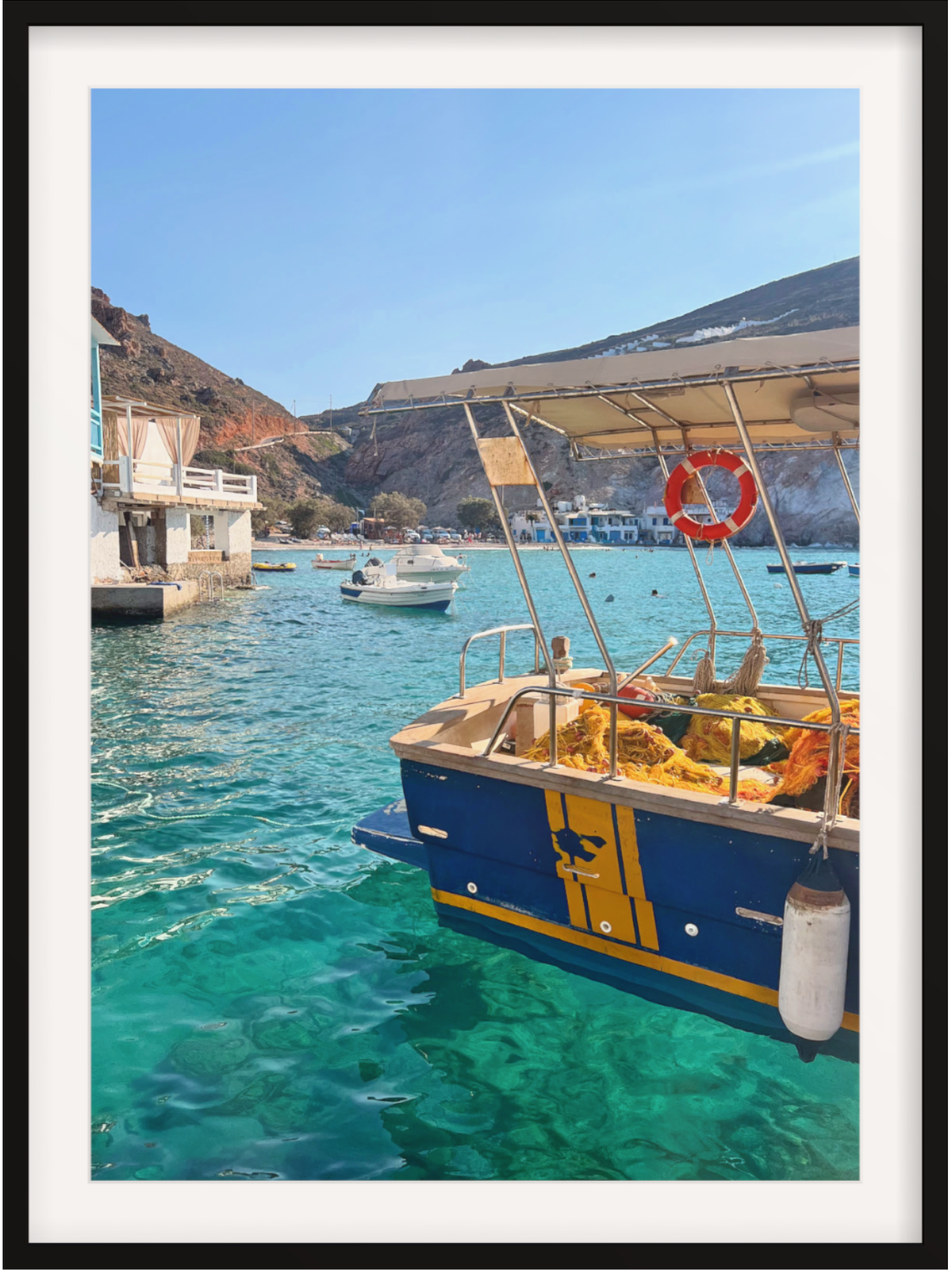 Framed photograph of a boat in a harbor with clear blue water and a mountainous background.