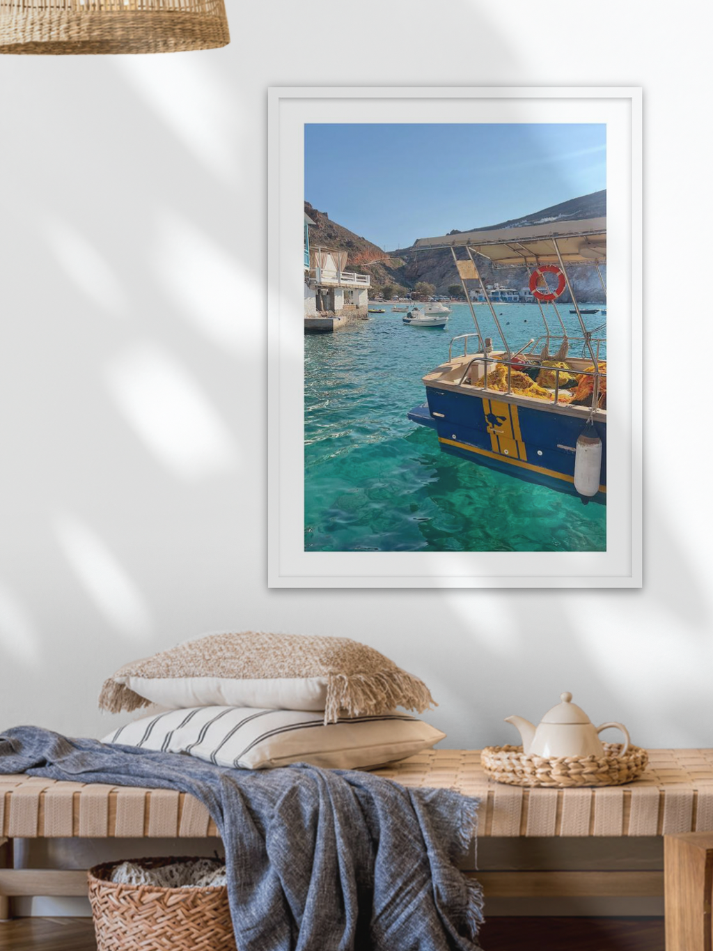 Framed photograph of a coastal scene with boats on a wall above a wooden bench.