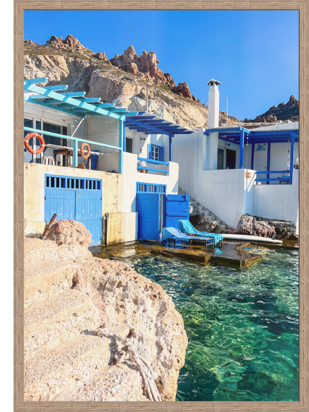 Greek island wall art in light wood frame featuring chimney and craggy cliffs