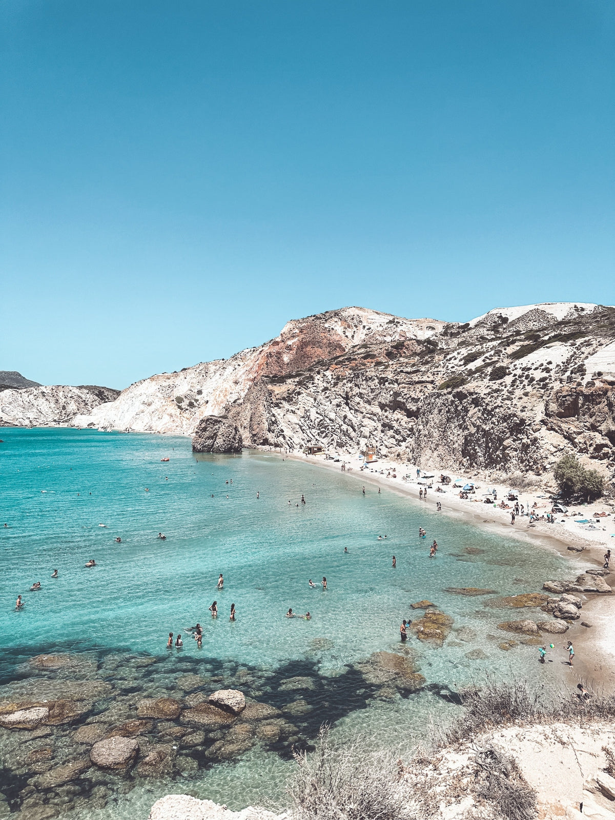 Beach with clear blue water and rocky cliffs under a bright blue sky
