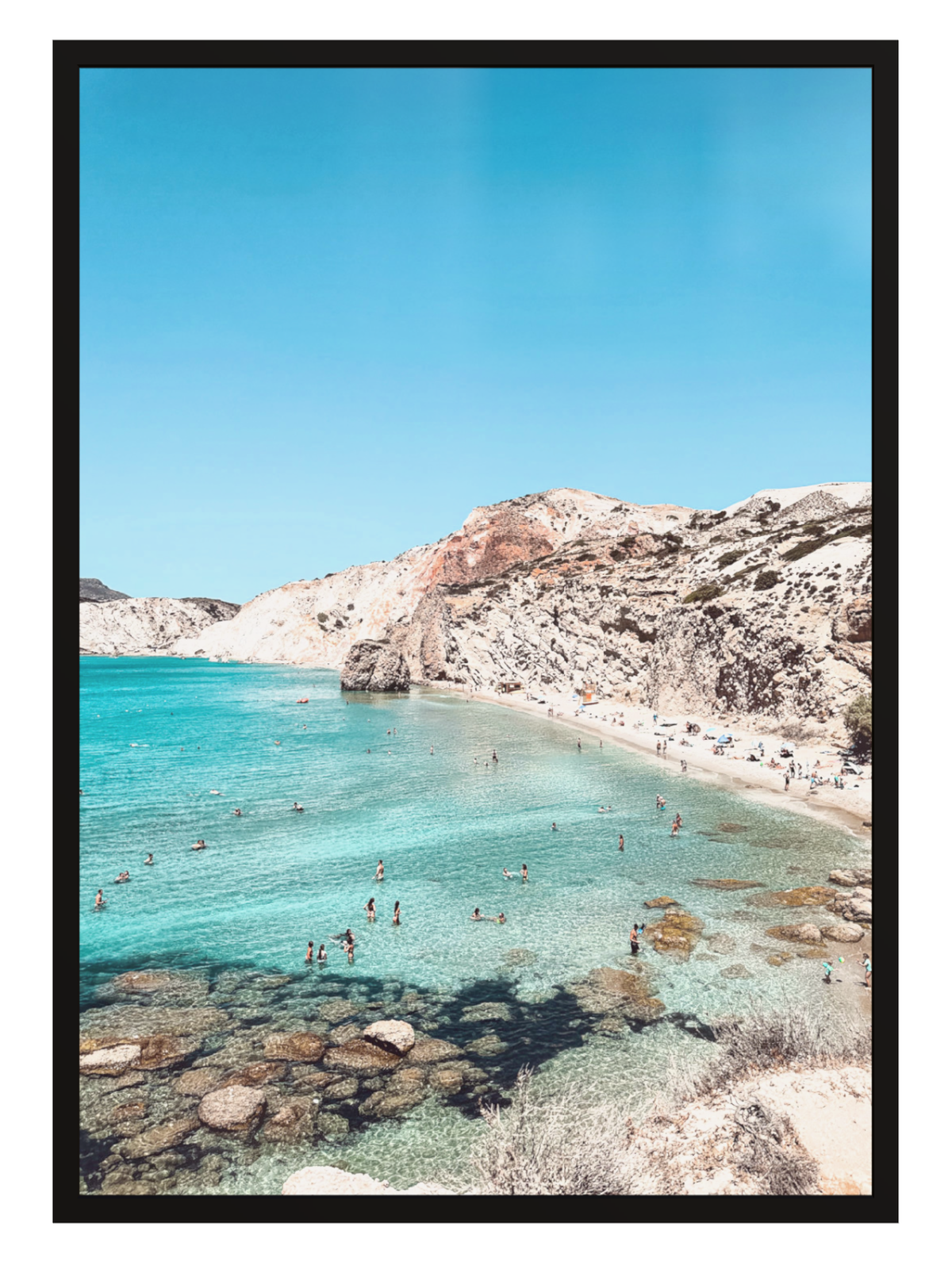 Beach scene with clear blue water and rocky cliffs under a bright sky