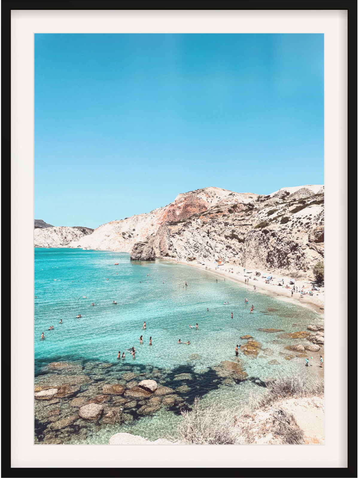 Beach scene with clear blue water and rocky cliffs under a bright sky.