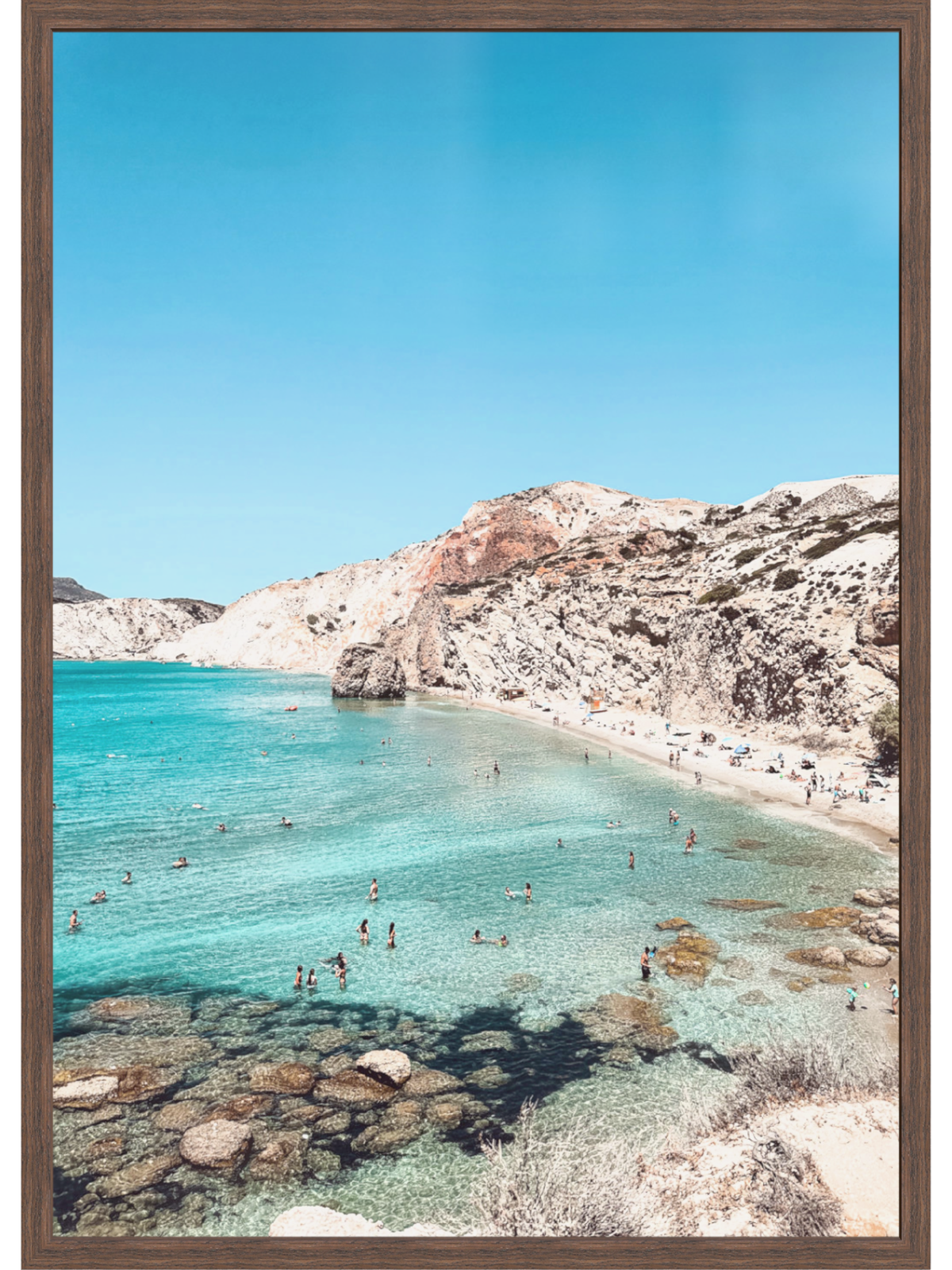 Beach scene with clear blue water and rocky shoreline, framed in brown.