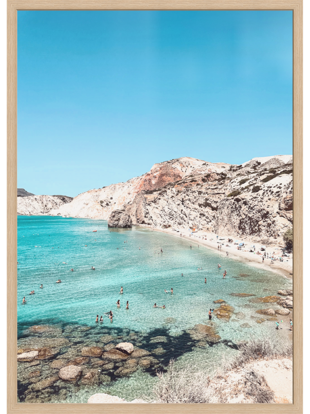 Beach scene with clear blue water and rocky cliffs under a bright sky.