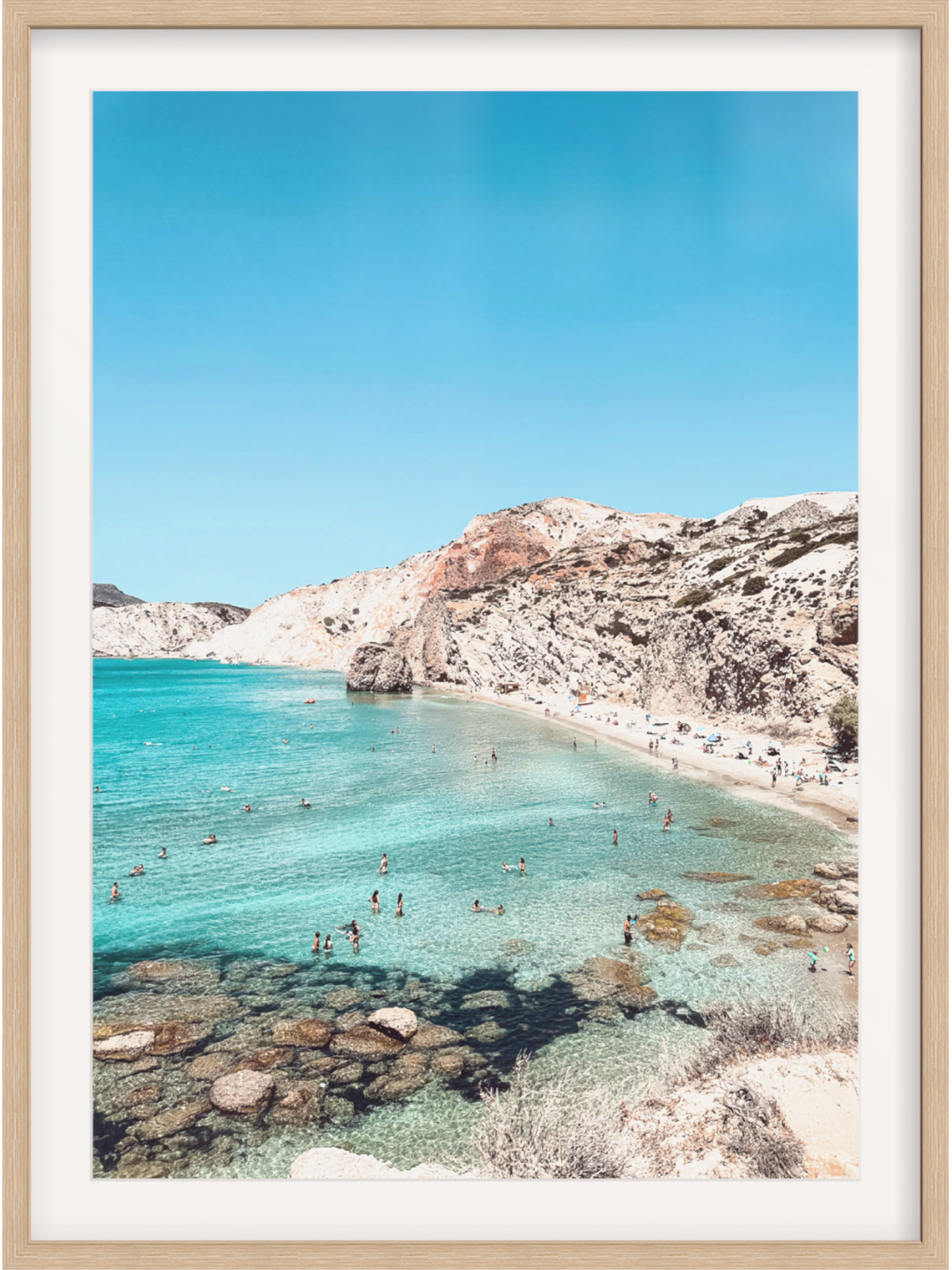 Framed photograph of a beach with clear blue water and rocky cliffs.