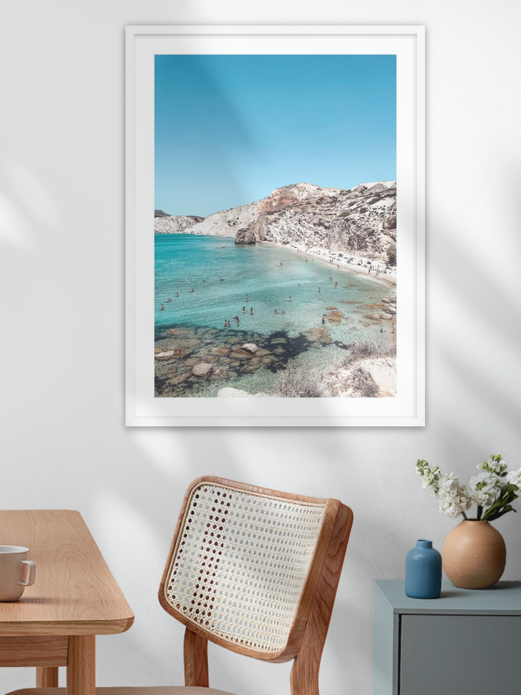 Framed beachscape print on a wall above a wooden table and chair.