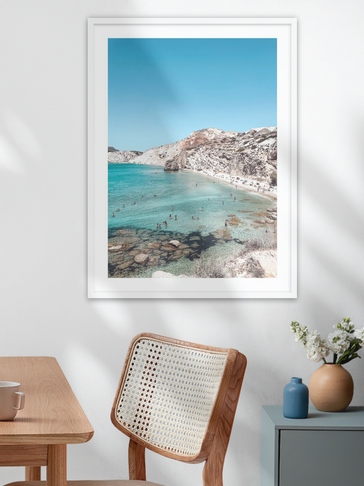Framed beachscape print on a wall above a wooden table and chair.