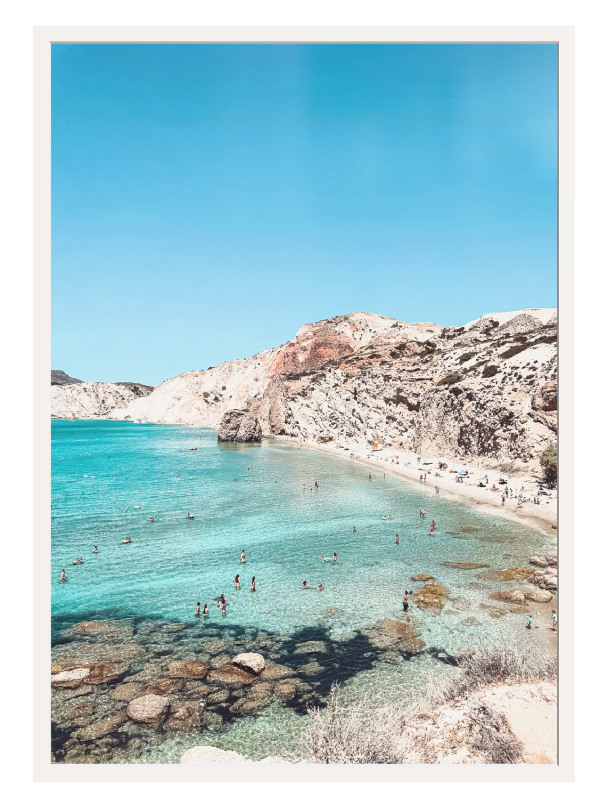 Beach scene with clear blue water and rocky cliffs under a bright blue sky.